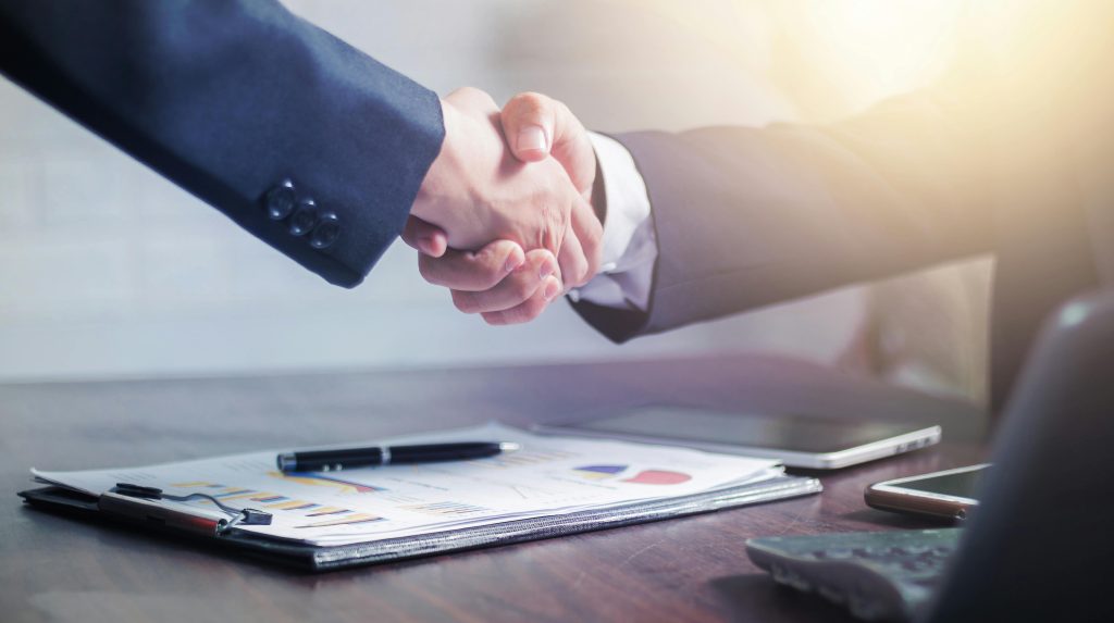 Current image: Professional handshake agreement over business charts in an office setting.